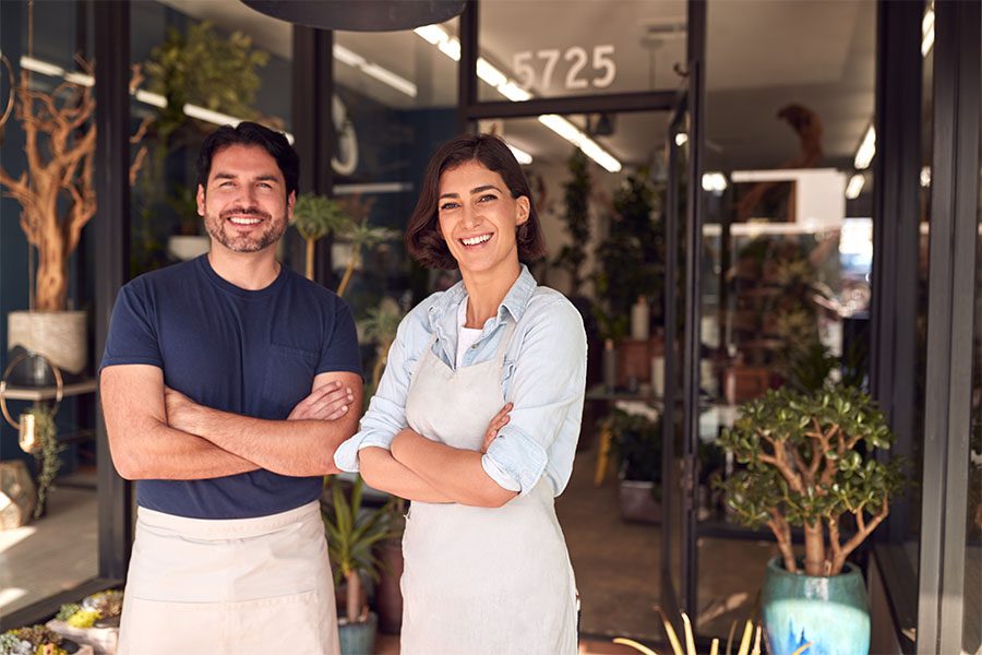 Business Insurance - Portrait of Two Cheerful Business Owners Standing Outside Their Flower Shop with Their Arms Crossed