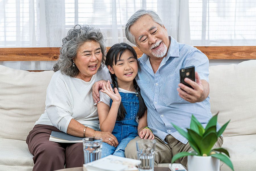 Contact - Cheerful Grandparents and Granddaughter Sitting on the Sofa Having Fun Using a Phone to Video Chat